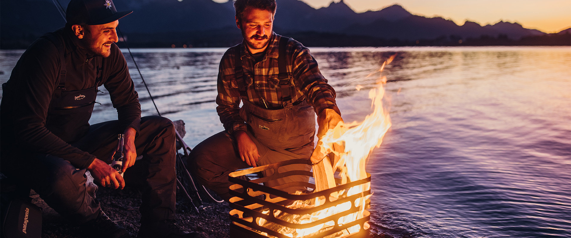 An image showing two men sitting around a fire on a lake