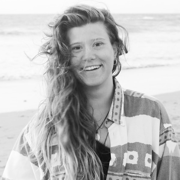 Une femme assise sur la plage avec ses cheveux au vent.