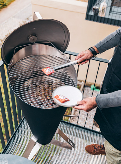 An inviting scene with a man grilling on a grill with a spat, highlighted by the presence of the Cone Charcoal Grill