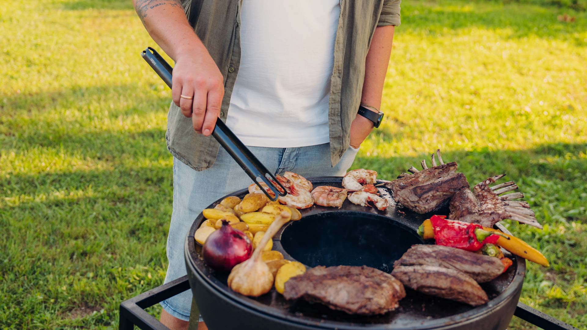 Die 00859 Tong Black fügt sich nahtlos in die Umgebung ein, wo ein Mann Essen auf einem Grill im Gras kocht.