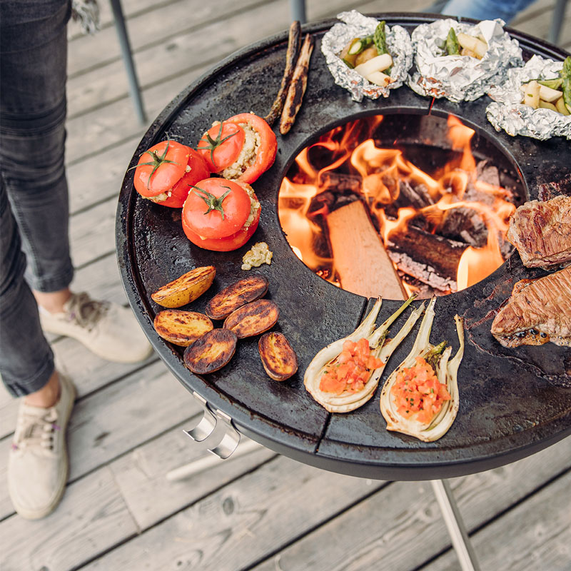 A depiction of a person is cooking food on a grill, featuring the Bowl 57 with starstand as a central and purposeful element.