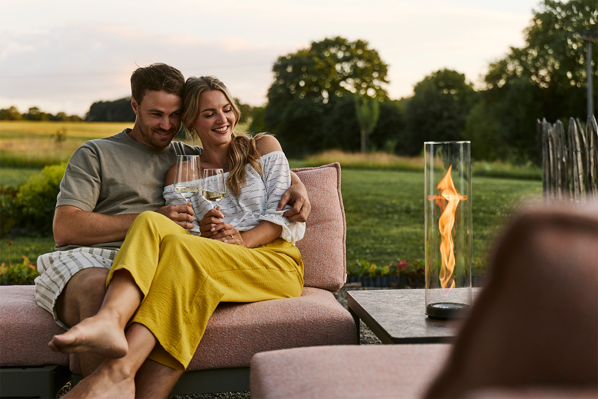 SPIN air 1200 Built-in Ein Paar sitzt zusammen auf Gartencouch und schaut in die Flamme von SPIN air Einbau im Beistelltisch.