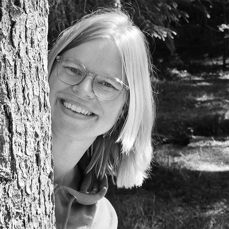 Une femme sourit derrière un arbre