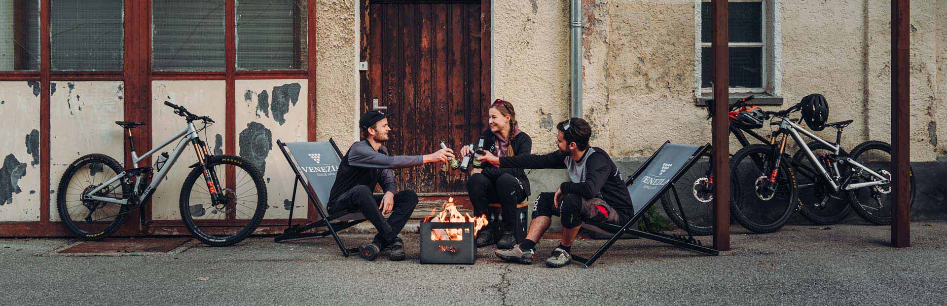 Depicted here is two people sitting around a fire pit, with the BEER BOX Fire Basket.