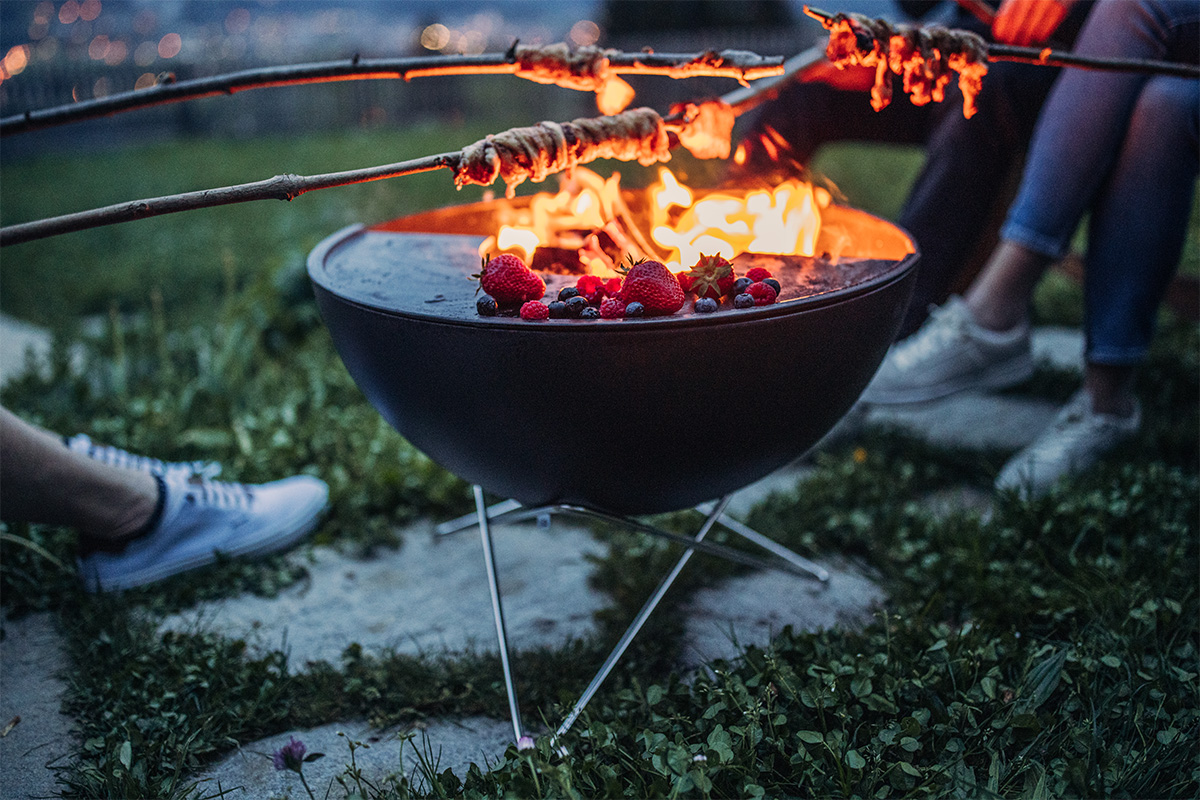 BOWL 57 Sternfuß Eine Person sitzt auf dem Gras, bereichert durch die Anwesenheit des 00343 Bowl 57 Star Ständers, der Design mit Funktionalität verbindet.