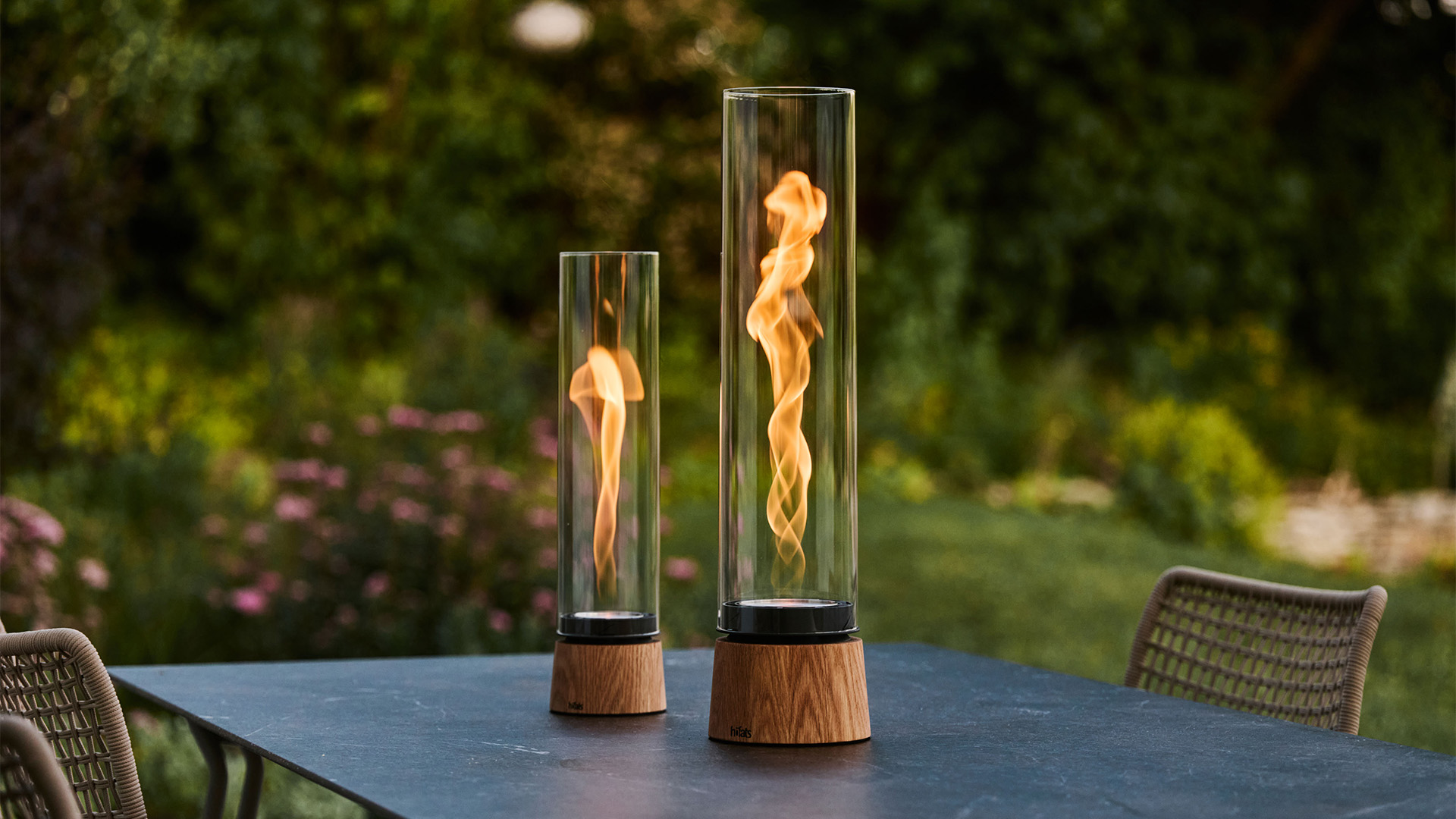 SPIN air 900 Eiche und SPIN air 1200 Eiche stehen nebeneinander auf Gartentisch, im Fokus die Flamme.