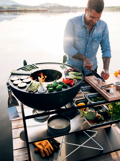 La BOWL FIRE KITCHEN est représentée par un homme qui cuisine sur un gril sur un quai, créant une image élégante et accessible.