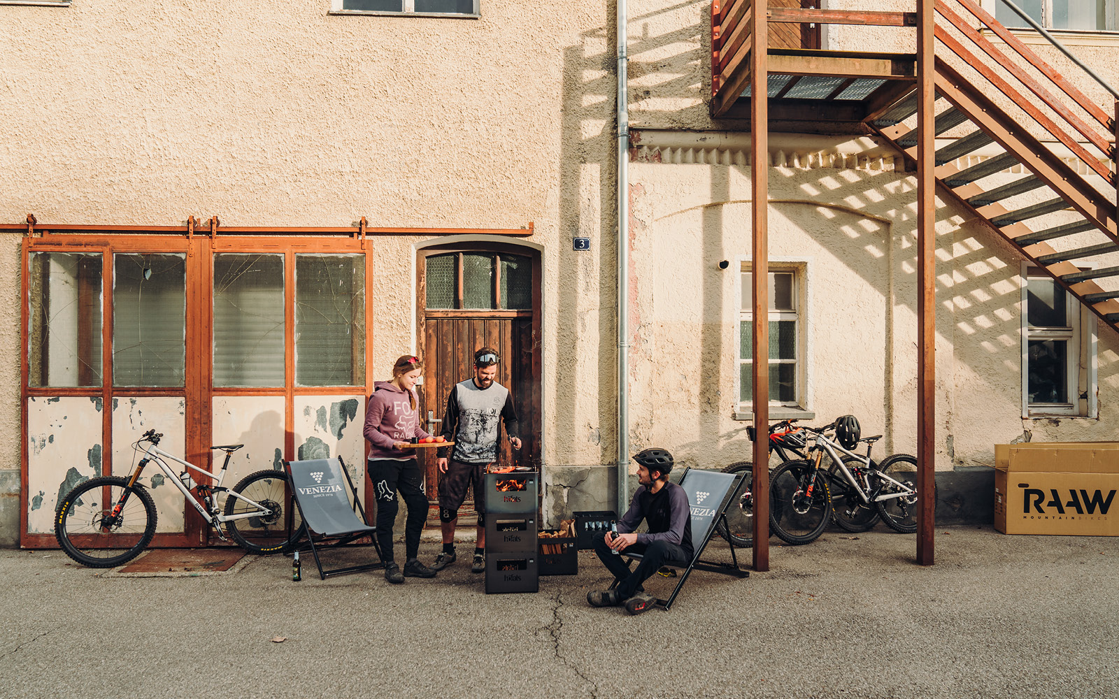 Illustrated is a man sitting on a chair in front of a building, with the BEER BOX Fire Basket.