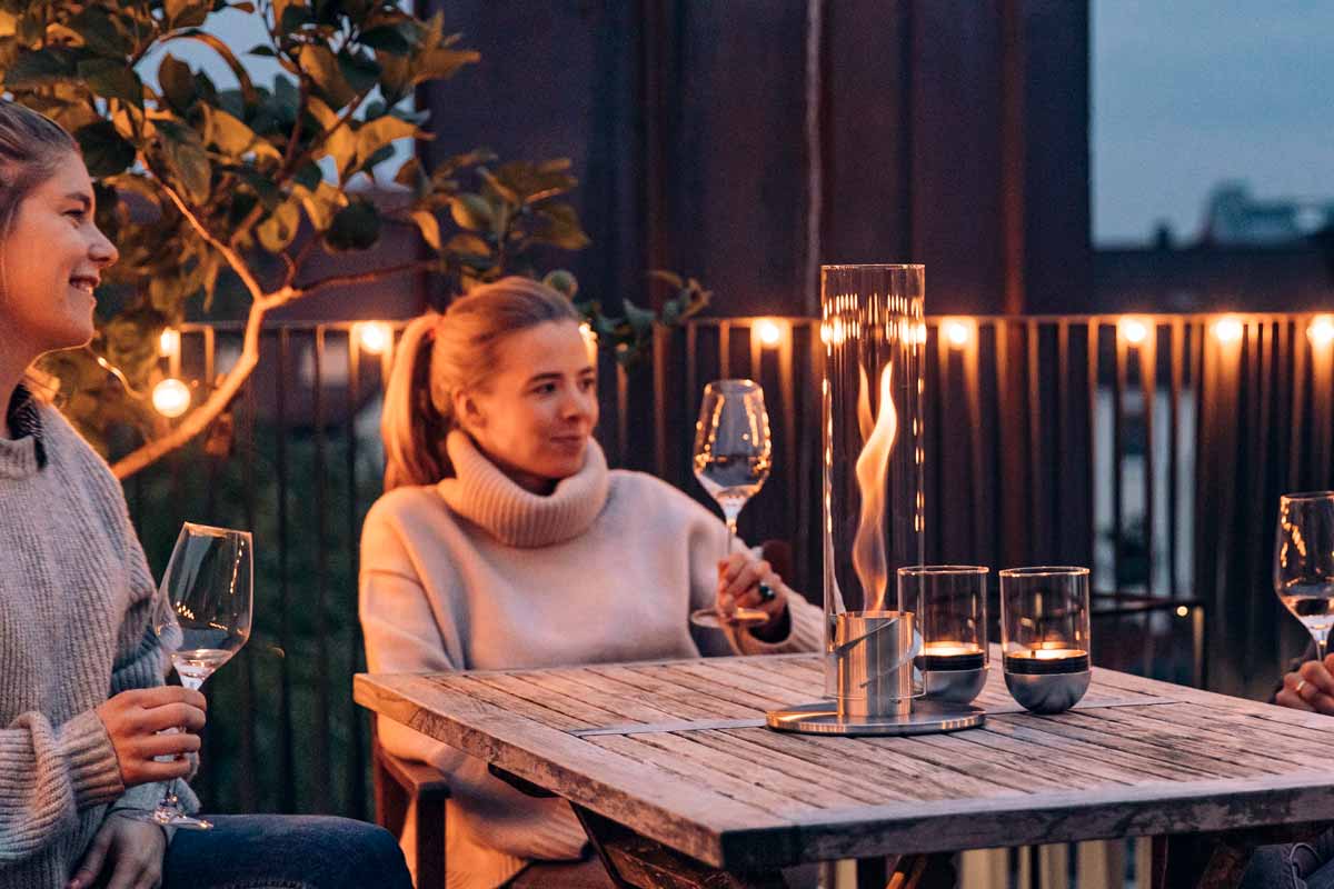 SPIN 120 Tischfeuer silber Szene, in der eine Familie bei Nacht zusammen an einem Tisch im Freien eine Mahlzeit genießt, wobei der Spin 90 Tischfeuer in Silber durch seine praktische Eleganz hervorsticht.