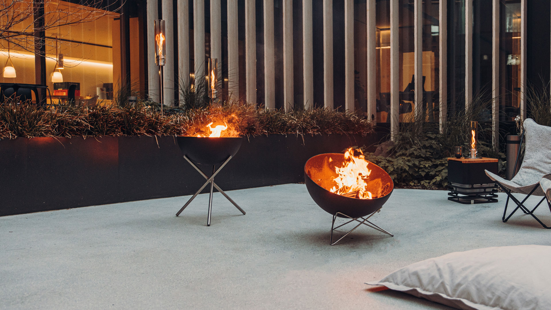 A view of a fire pit in a room with a bed and a chair, with the BOWL Fire Set flex.