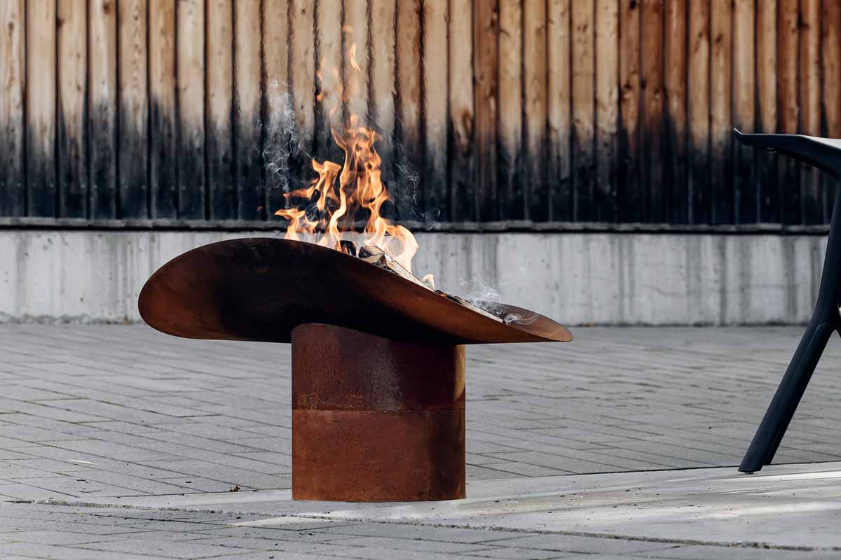 ELLIPSE Fuß Hier ist eine Feuerstelle mit einem Stuhl und einem Tisch abgebildet, mit der ELLIPSE Feuerschale.