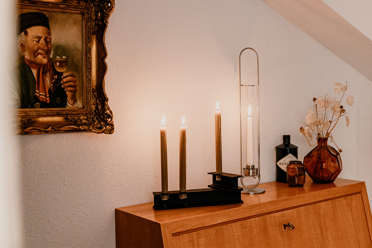 HENRY METAL I+II Kerzenhalter-Set schwarz Ein Bild zeigt ein Gemälde eines Mannes an der Wand, mit dem HENRY METAL II Kerzenhalter in Schwarz.