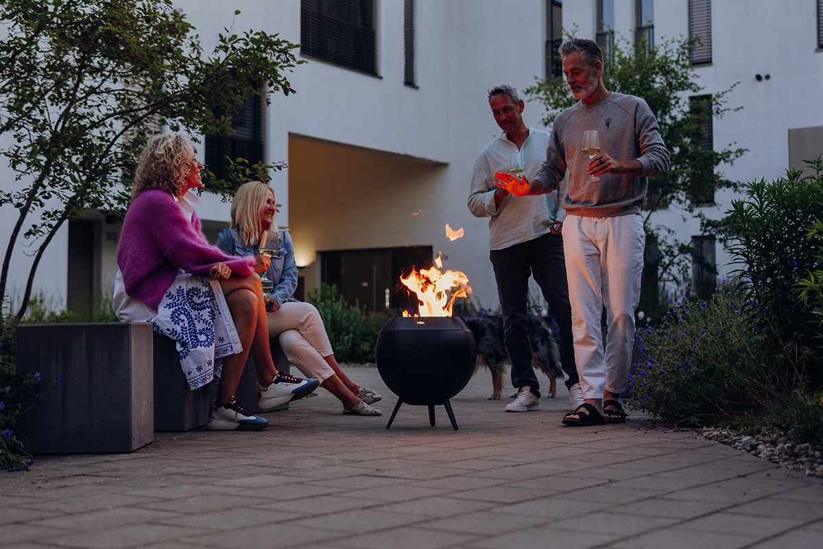 MOON 45 all black Fire Basket with low stand Vier Personen sitzen und stehen um die wärmende Feuerschale MOON.