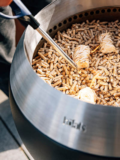 Une personne allume des copeaux de bois dans un brasero. Montrant comment allumer le MOON 45.