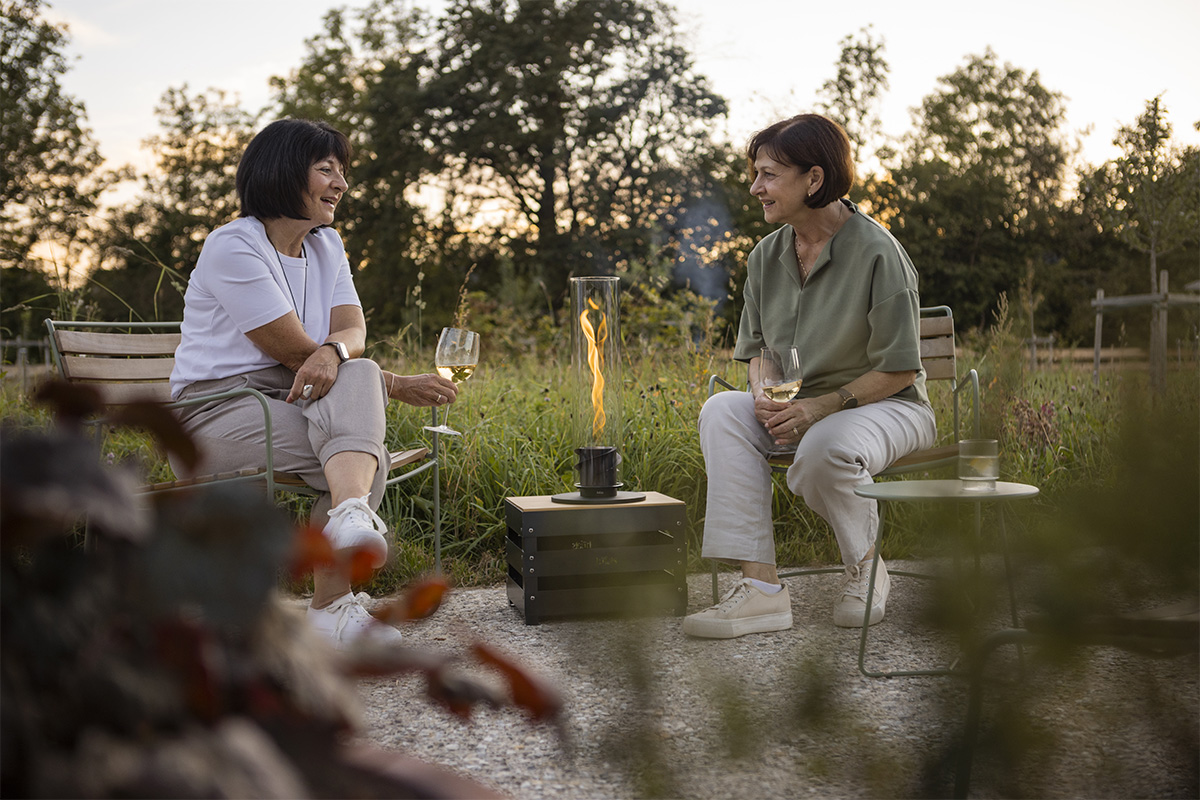 SPIN 900 Tabletop Fireplace black The 00700 Spin 1200 Tablefire black integrates seamlessly into the setting, where two people sitting on a bench.