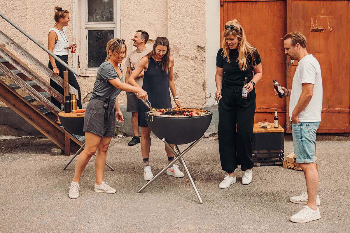 Depicted here is a group of people standing around a grill, with the BOWL 70 Tripod.