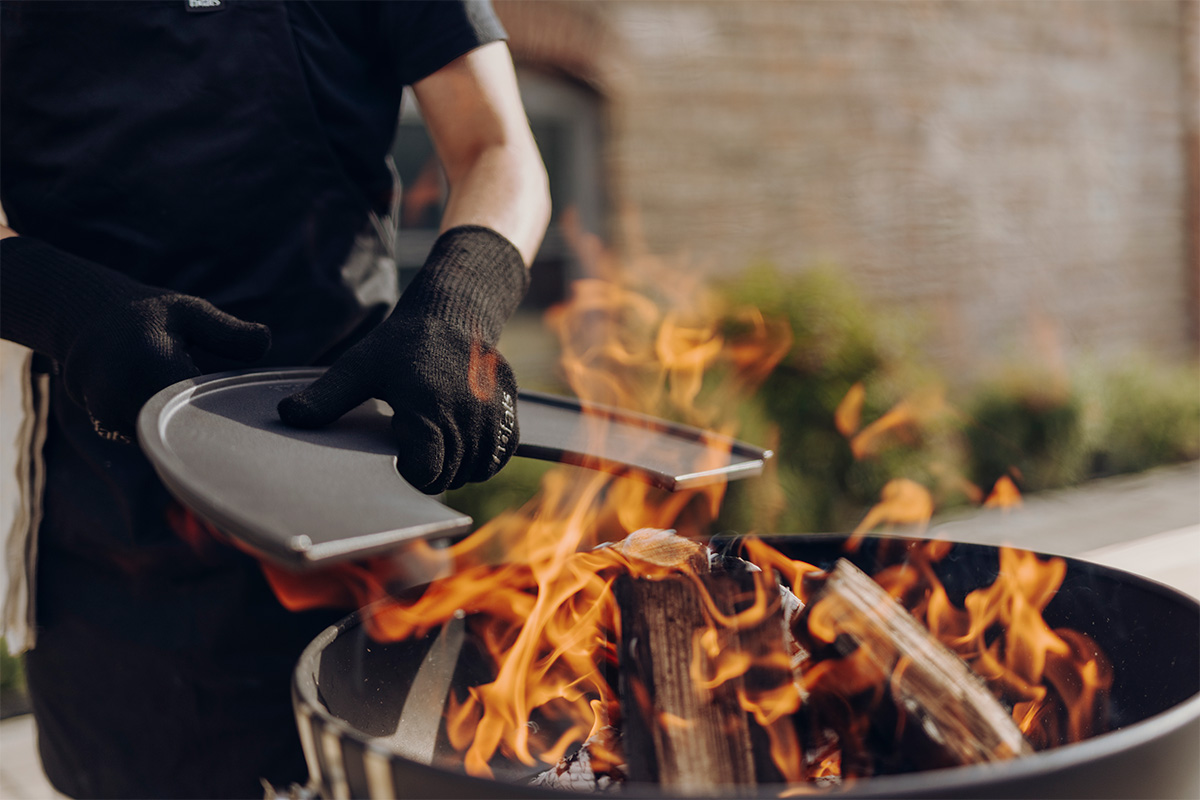 Feuerhandschuhe Aramid Ein Bild zeigt eine Person, die auf einem Grill mit einem Spatel kocht, mit den Feuerhandschuhen Aramid.