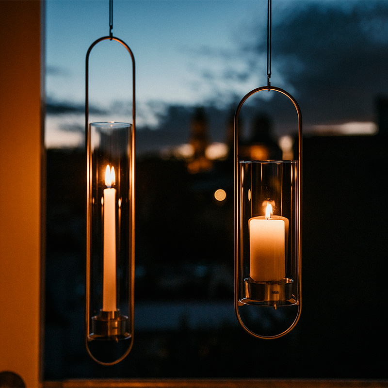 Deux bougies suspendues à une fenêtre, la OVAL CANDLE complète le moment avec son design réfléchi.