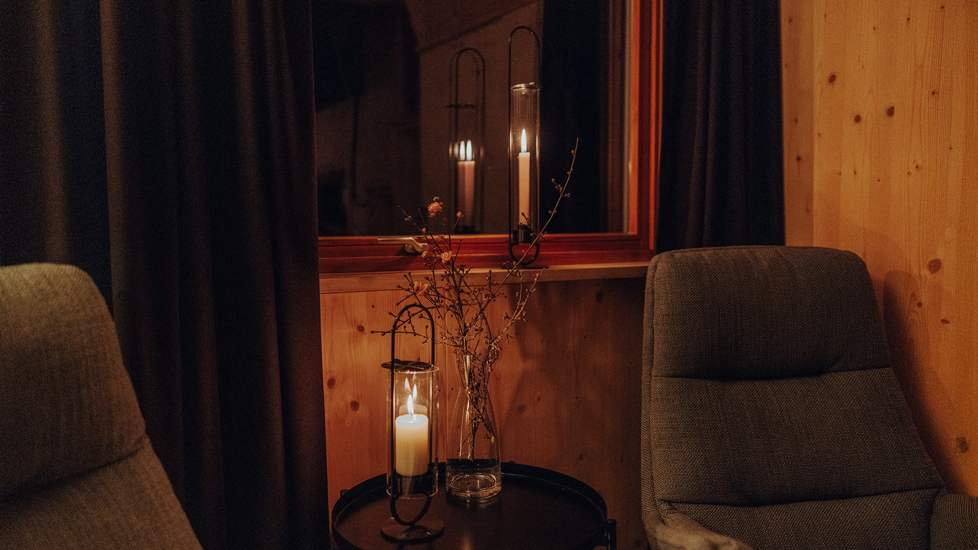 A depiction of a chair and a table with a candle on it, featuring the 00273 Oval Candle 35 black as a central and purposeful element.