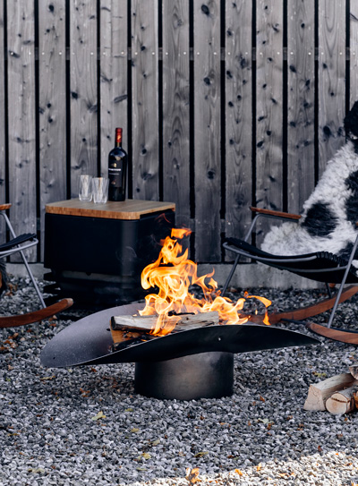 Une chaise à côté d'un brasero, le bol à feu 060101 ELLIPSE complète le moment avec son design réfléchi.
