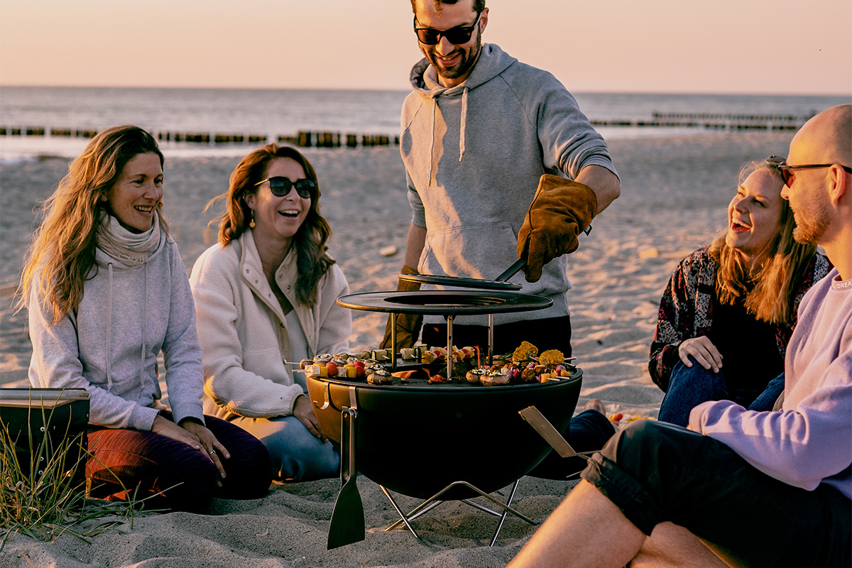 BOWL 57 Sear Grate Auf dem Bild sind Menschen am Strand zu sehen, mit dem BOWL 57 Wärmering.
