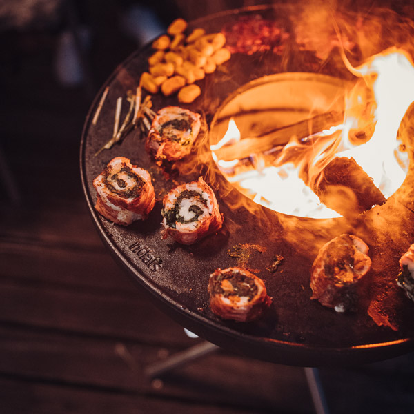Illustrated is a person holding a pan with food on it, with the BOWL Fire Bowl.