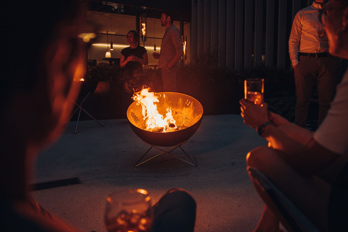 This image shows a group of people sitting around a fire pit, with the BOWL 70 Tripod.