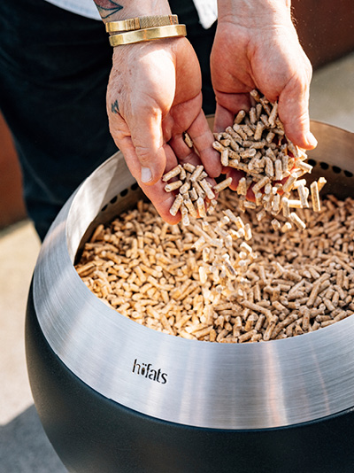 Une personne met des copeaux de bois dans un Brasero. Montrant comment allumer le MOON 45.