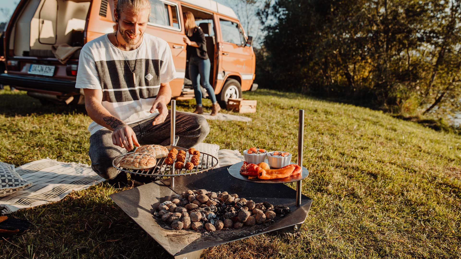 A man sitting on the grass in front of a van with food, with the Triple pole adding a functional and elegant touch to the scene.