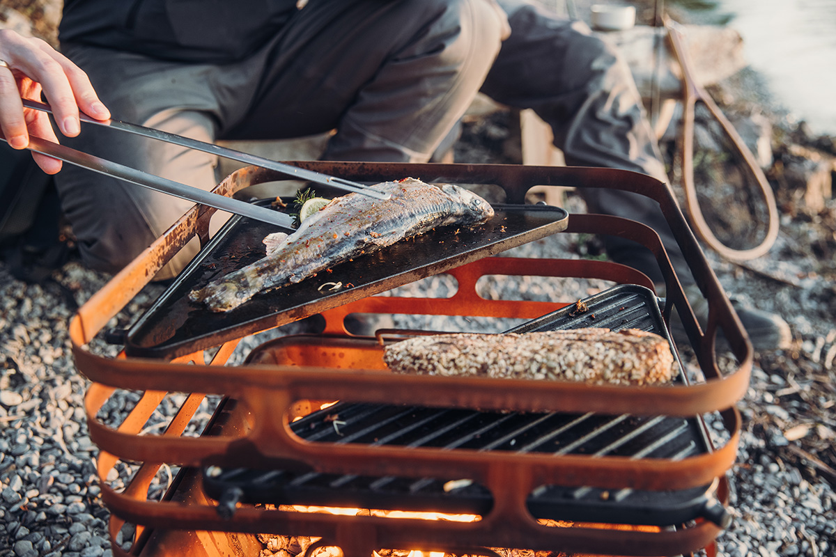 La photo présente une personne en train de cuisiner de la nourriture sur un grill, avec la Plancha CUBE.