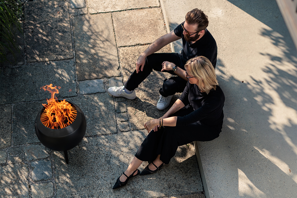 Bild aus der Vogelperspektive. Zwei Personen schauen auf einer Terrasse sitzend in die lodernde Flamme von MOON. Bild aus der Vogelperspektive. Zwei Personen schauen auf einer Terrasse sitzend in die lodernde Flamme von MOON.