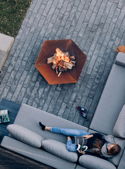 Eine Frau liegt auf einer Couch neben einem Kamin, wobei der Triple-Kamin eine funktionale und elegante Note zur Szene hinzufügt.