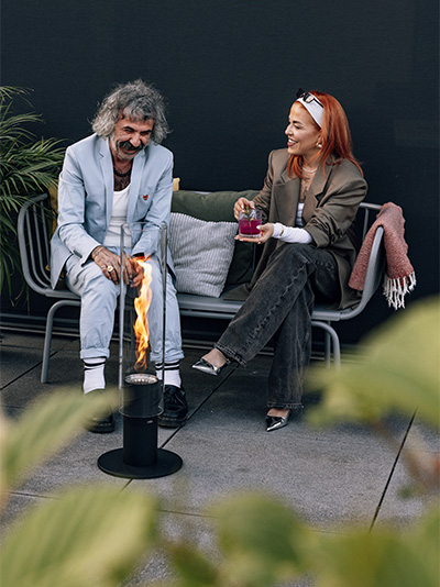 Une femme assise sur un banc et la cheminée sur pied SPIN 1500 complète le moment avec son design réfléchi.
