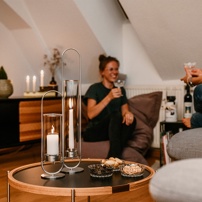 Une représentation d'un couple assis sur un canapé dans un salon, mettant en vedette la OVAL CANDLE comme élément central et utile.