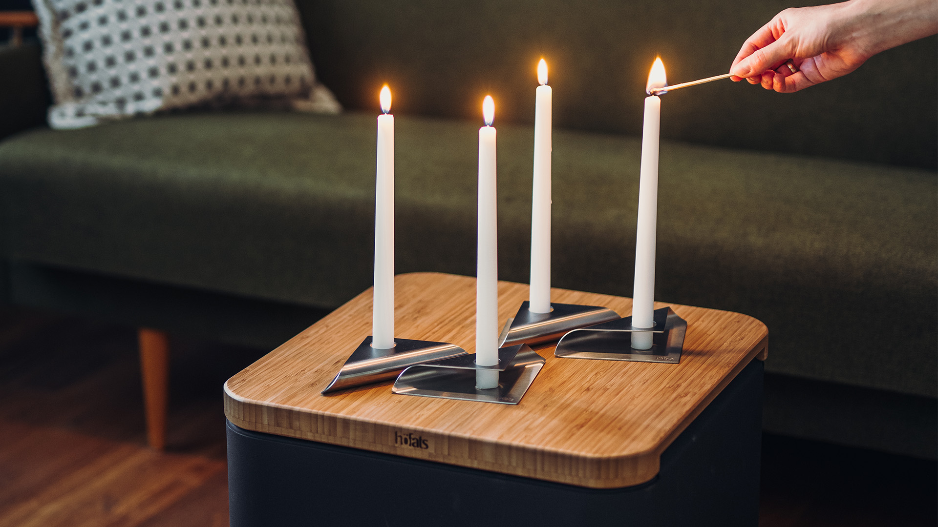 On voit ici une personne allumer une bougie sur une table, avec la SQUARE CANDLE .