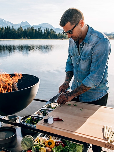 Cette image montre un homme en train de cuisiner sur un grill, avec la FIRE KITCHEN.