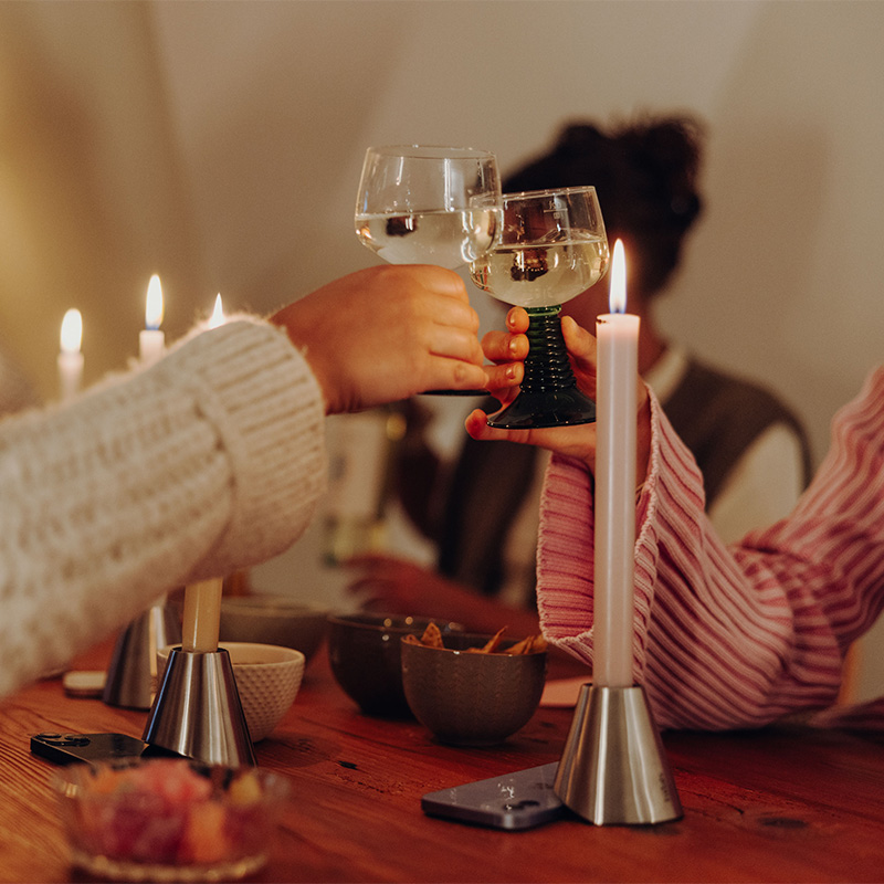 Drei Digi Detox mit Smartphone darunter auf Küchentisch. Daneben zwei Hände die mit einem Weinglas anstoßen.