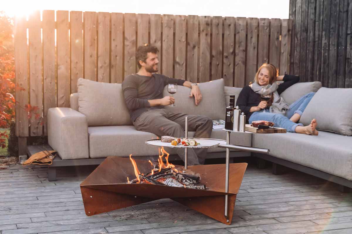 TRIPLE Grid 55 A man and woman sitting on a couch by a fire pit, enriched by the presence of the Triple Grid 55, which merges design with utility.