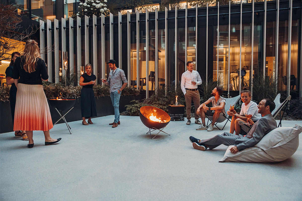 BOWL 70 Sternfuß Eine Gruppe von Menschen sitzt auf einer Terrasse, wobei der 00259 Bowl 70 Sternfuß eine funktionale und elegante Note zur Szene hinzufügt.