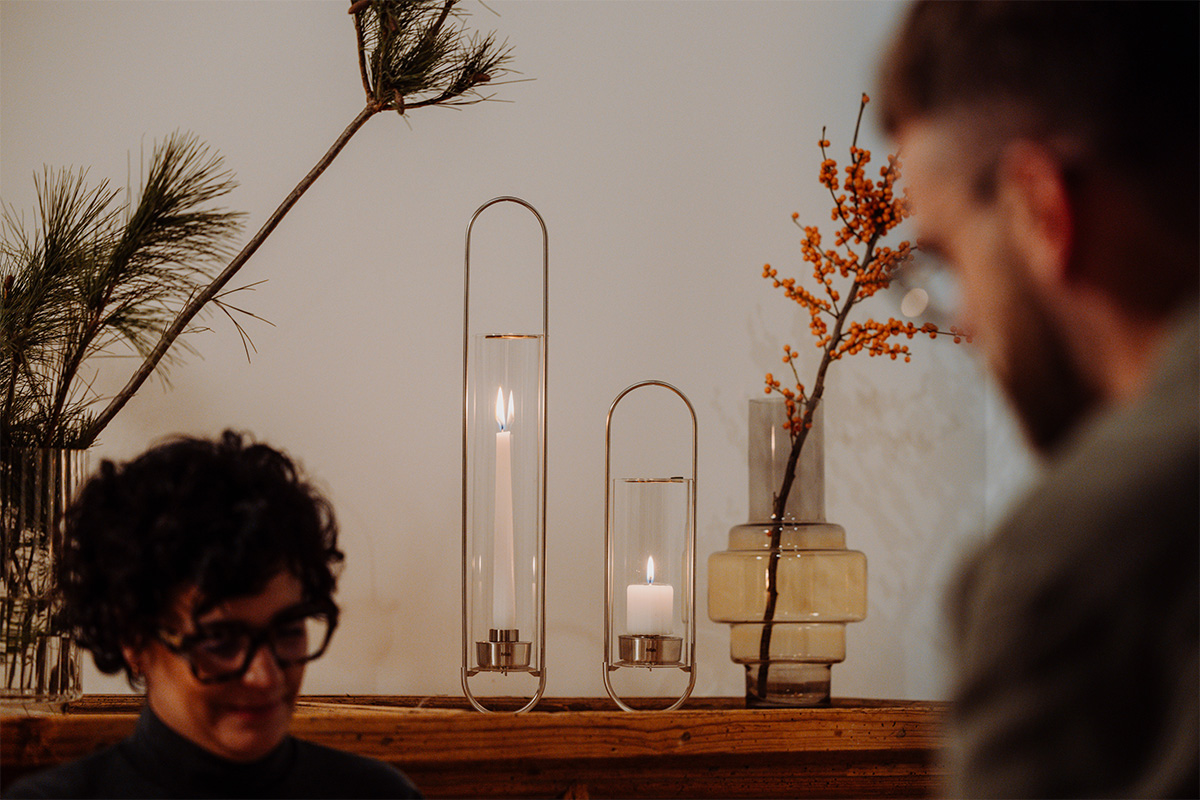 Une représentation d'un homme assis devant une table avec un vase et une bougie, mettant en vedette la OVAL CANDLE 55 comme élément central et utile.
