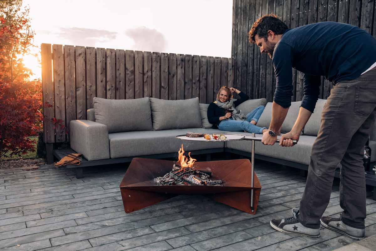 The Triple Grid 55 integrates seamlessly into the setting, where a man and woman are setting up a fire pit.