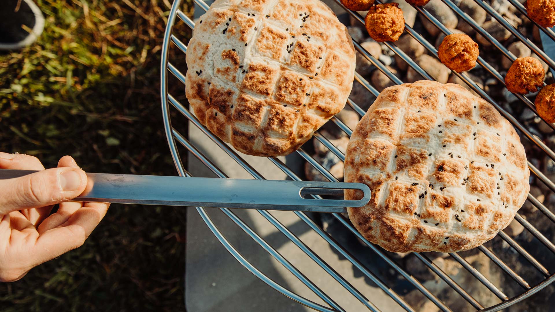 Eine Darstellung einer Person, die auf einem Grill Essen zubereitet, wobei das Triple 65 Fireplace BBQ Set als zentrales und zweckmäßiges Element dargestellt ist.