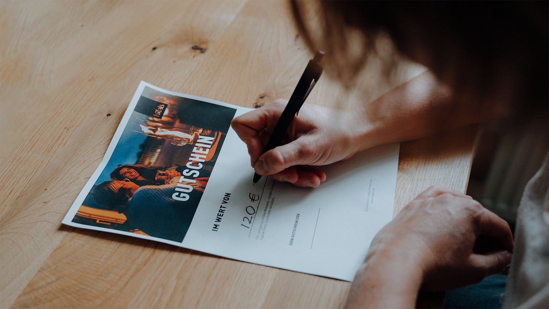 Cette image montre une personne écrivant sur un morceau de papier, avec le BON CADEAU numérique.