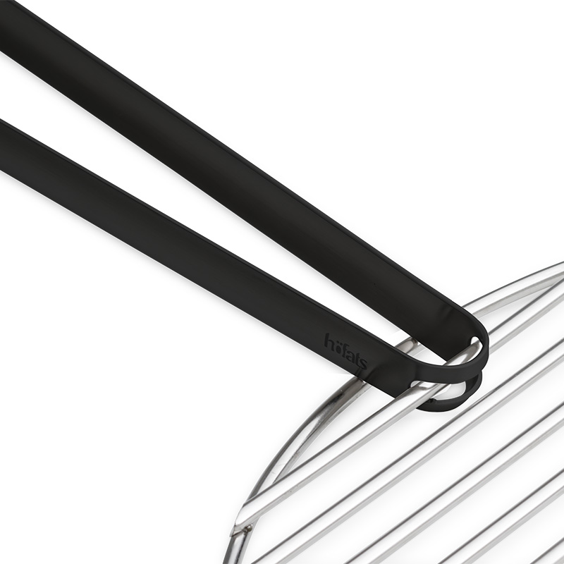 Grillzange schwarz Die 00859 Grillzange wird als schwarze Metallzange dargestellt, die an einem Stahlrost befestigt ist und so ein stilvolles und zugängliches Bild erzeugt.