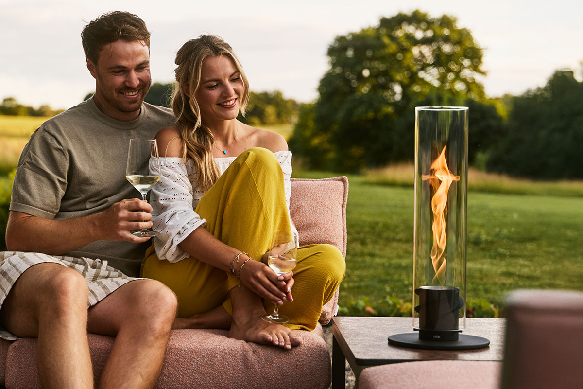 SPIN 900 Tabletop Fireplace black Ein Paar sitzt zusammen auf Gartencouch und schaut in die Flamme von SPIN air Einbau im Beistelltisch.