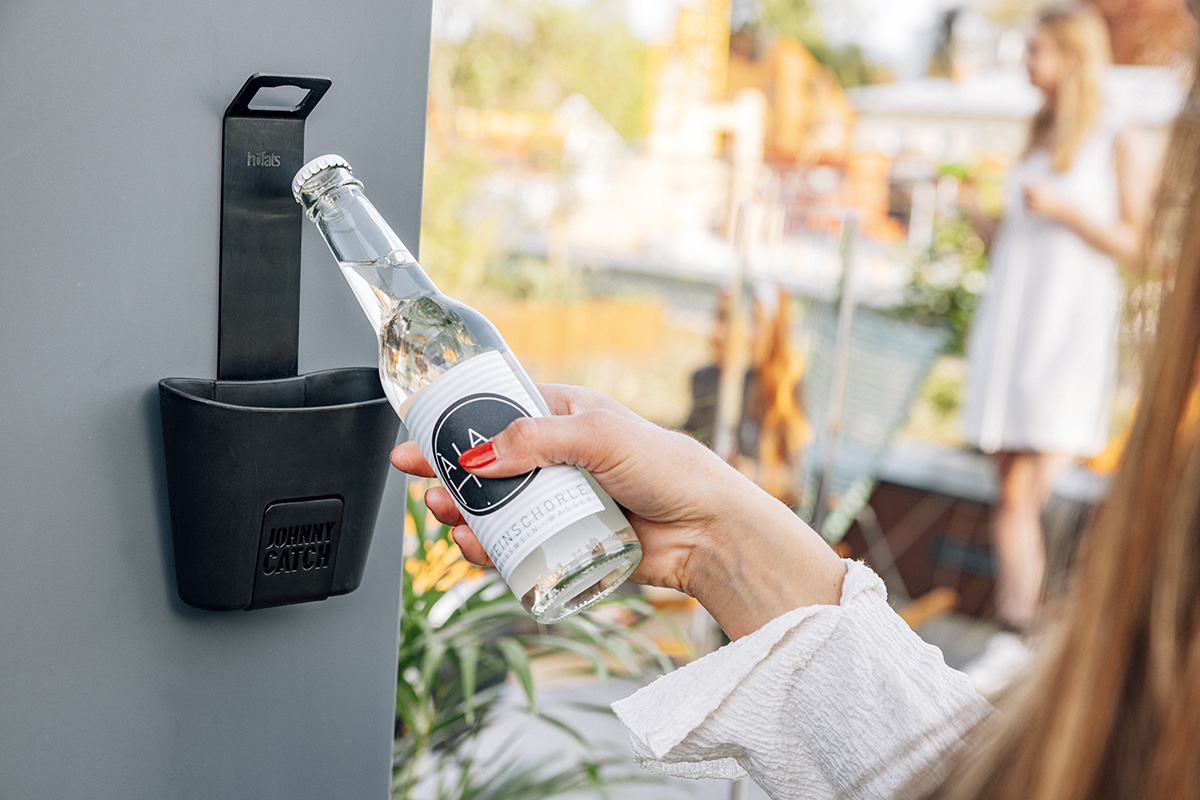 Die Darstellung einer Frau, die eine Wasserflasche öffnet, wobei der 00842 Johnny Catch Cup Black Bottleopener als zentrales und zweckmäßiges Element dient.