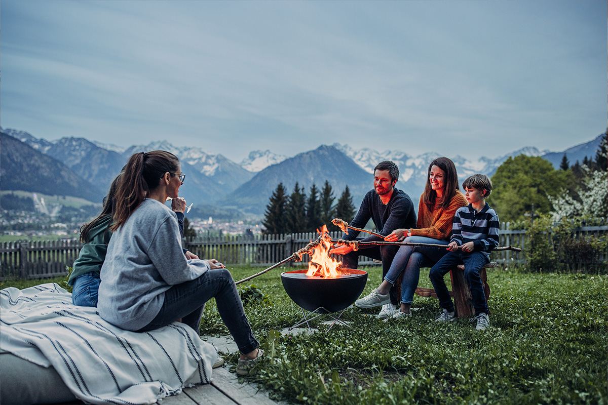 Une femme et deux enfants assis autour d'un brasero, avec le bol 00249 BOWL 57 avec support étoile ajoutant une touche fonctionnelle et élégante à la scène.