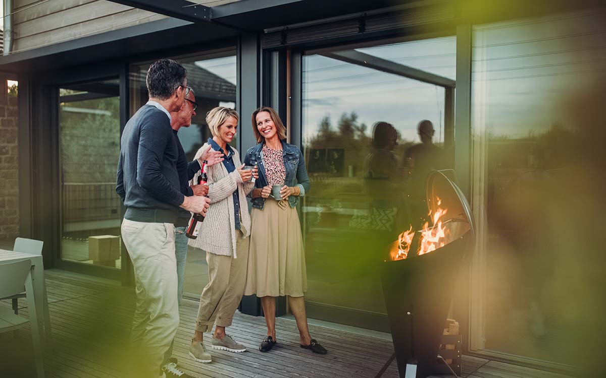 Ein Bild, das ein Paar zeigt, das auf einer Terrasse neben einem Feuer steht.