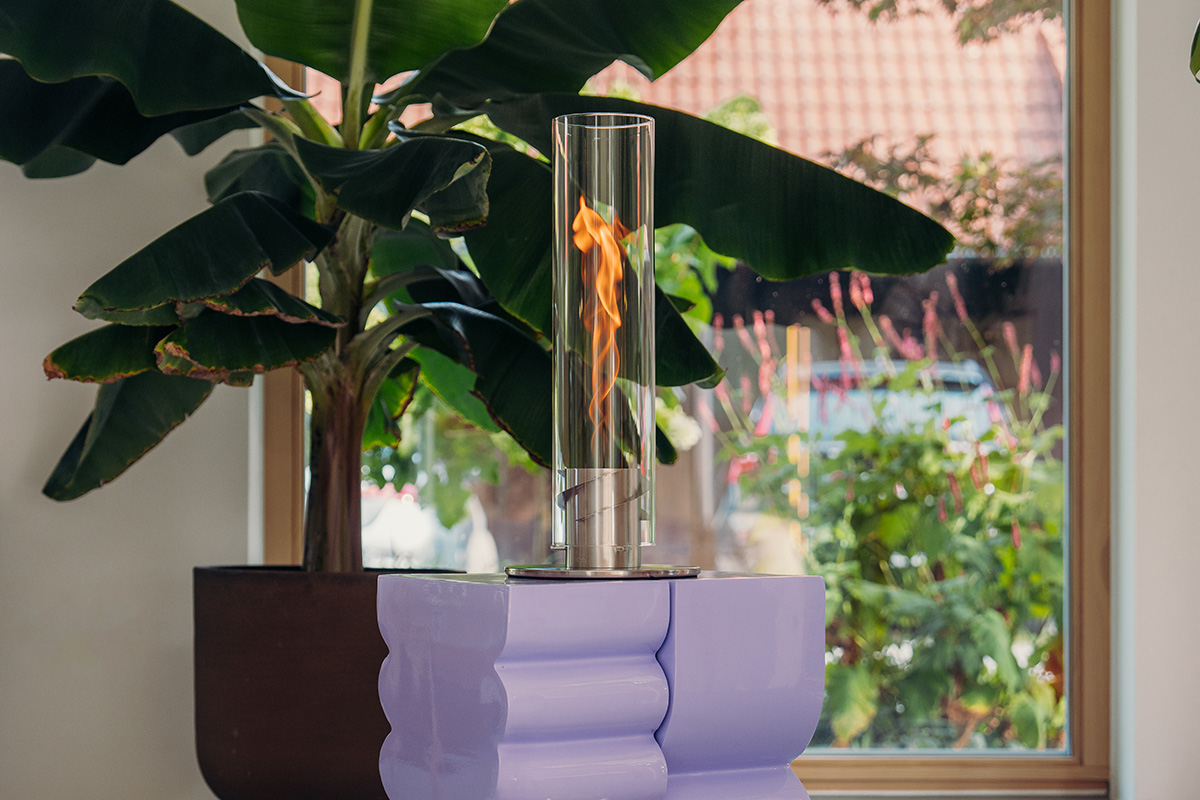 An inviting scene with a banana plant stands behind a SPIN Tablefire, highlighted by the presence of the 00695 Spin 1200 Tablefire silver