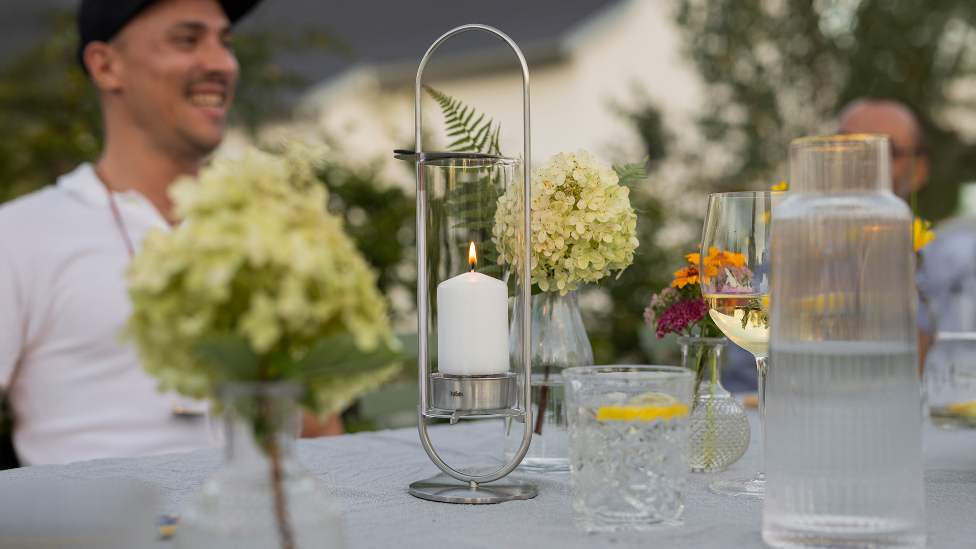 Erleben Sie einen Mann, der an einem Tisch mit Blumen und Kerzen sitzt, mit dem raffinierten Touch der 00271 Oval Candle 35.